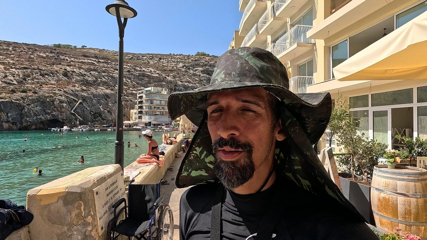 Ramon diante da água e dos edifícios de Xlendi, em Gozo